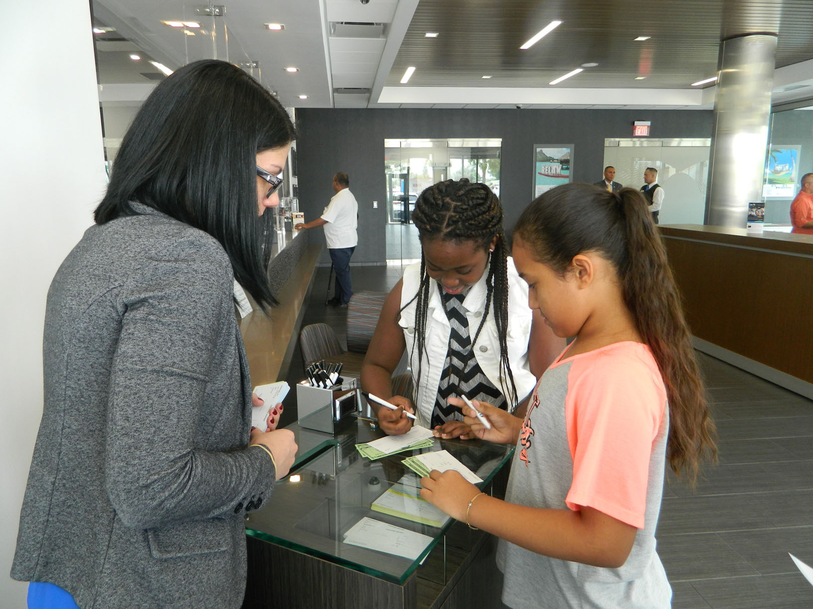 BankUnited Learning & Development Facility Trainer Meghan Bussell helps students Dayna-Lee Polo and Ivanna Matta fill out deposit tickets. 